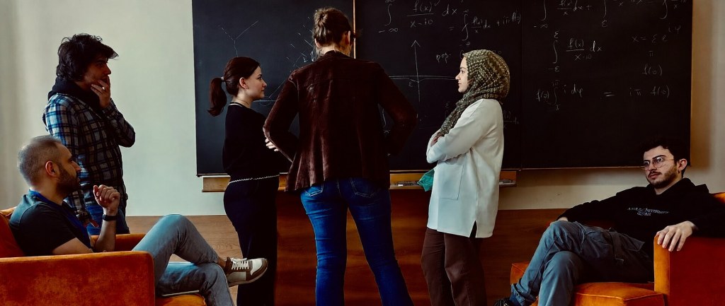 Students and researchers discussing theoretical physics in front of a blackboard